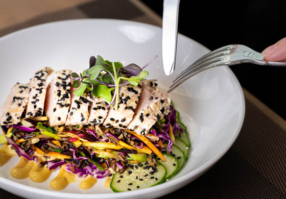 Fork and knife cutting into a tuna albacore poke bowl at Stratus Restaurant